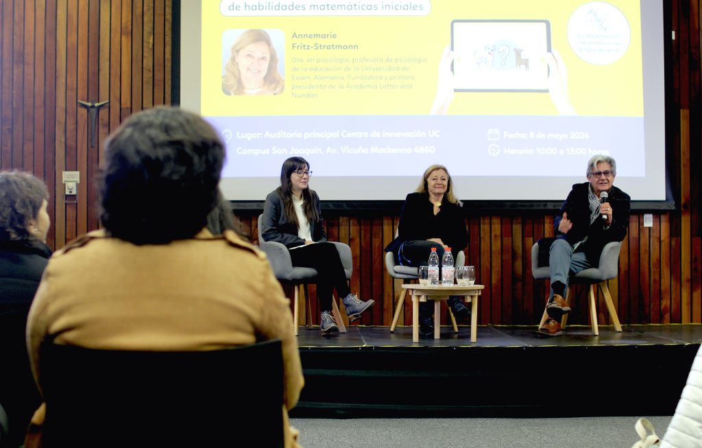 Fotografía del escenario en el lanzamiento de MARKO-D. De izquierda a derecha, se encuentran Victoria Espinoza, Annemarie Fritz, y Ricardo Rosas, sentados y respondiendo preguntas al público. Arriba de ellos está la pantalla de proyección del lanzamiento. 