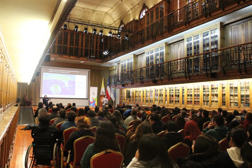 imagen en donde se ve una toma desde atrás de un auditorio en donde hay un grupo amplio de personas mirando hacía una presentación adelante