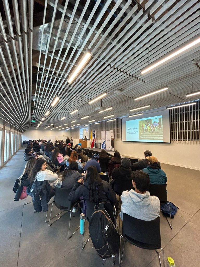 imagen en donde se ve desde atrás a varias personas sentadas en un auditorio mientras expone Nieves Peinado. 