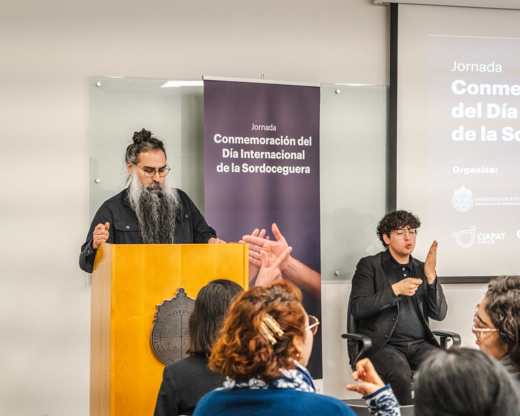 imagen en donde aparece el locutor, Francisco Pizarro, en un podio y al lado se encuentra el intérprete en lengua de señas.