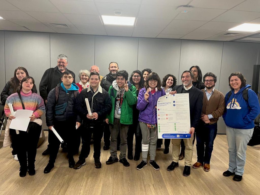 imagen en la que se aprecia a un grupo de personas mirando hacía la cámara con un póster de accesibilidad cognitiva.