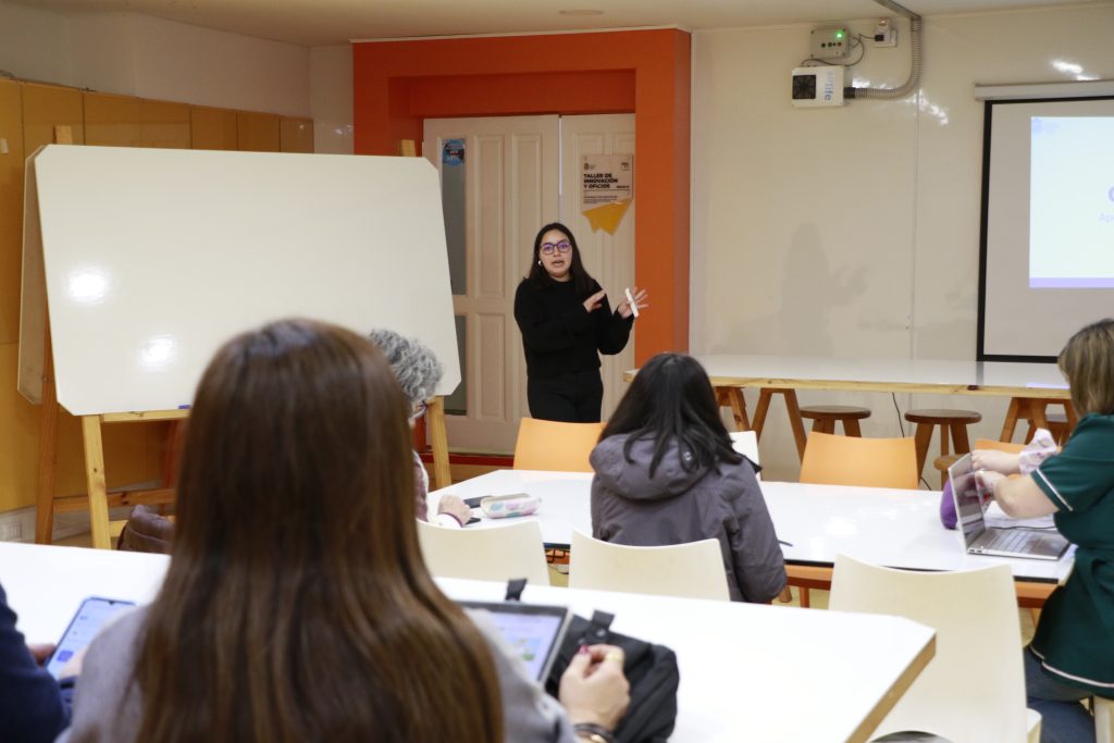  imagen en donde aparece una toma desde atrás en donde hay varias personas sentadas mirando adelante de un salón a Camila Cachaña que se encuentra hablando. 